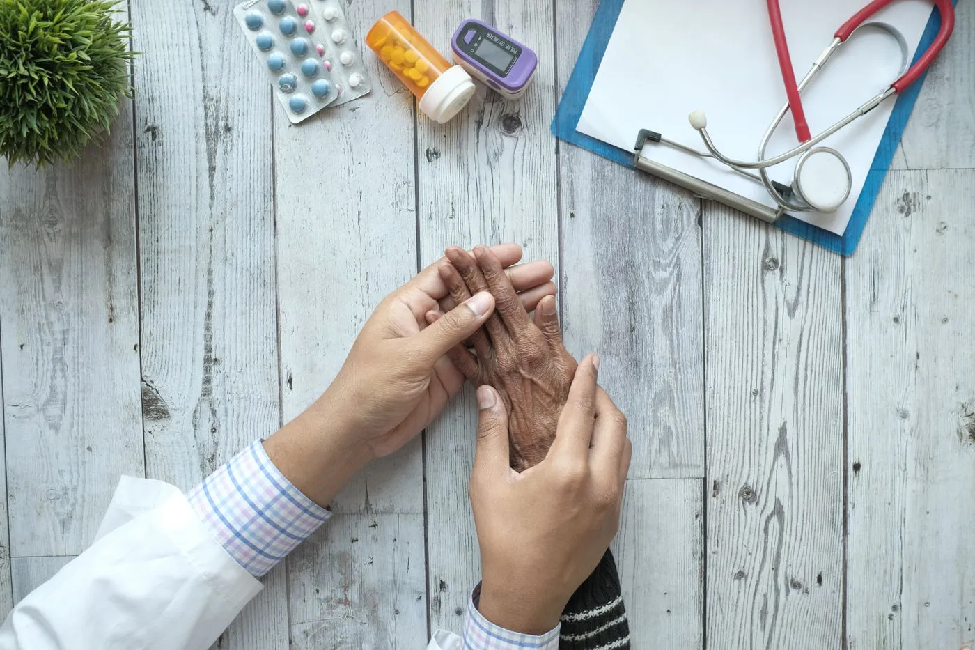 A clinician gently holding an older patient’s hands across a desk