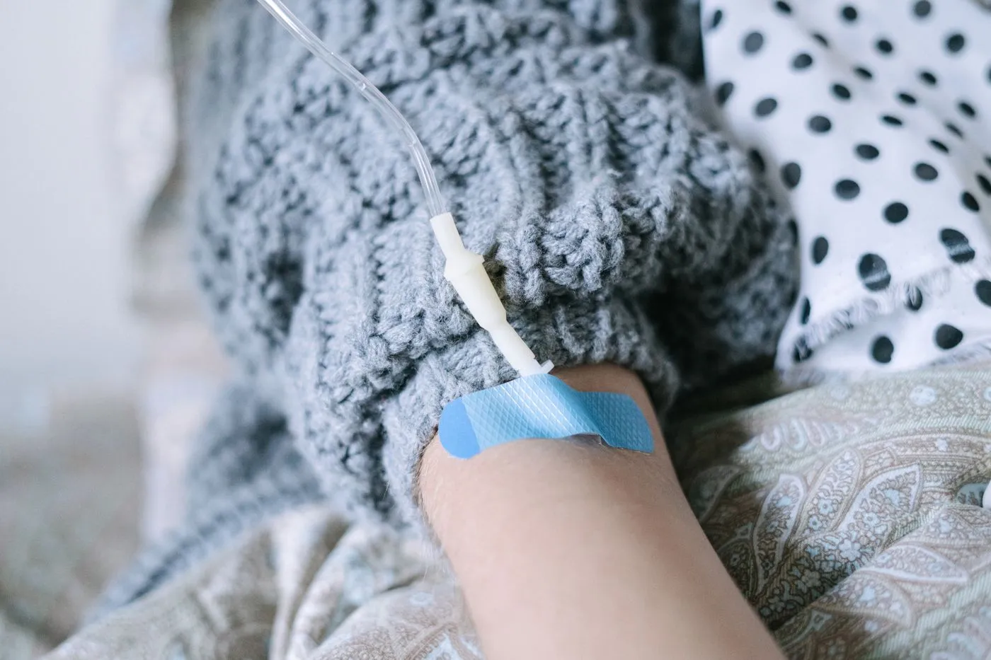 A patient resting under a blanket with an IV line taped in place during an infusion